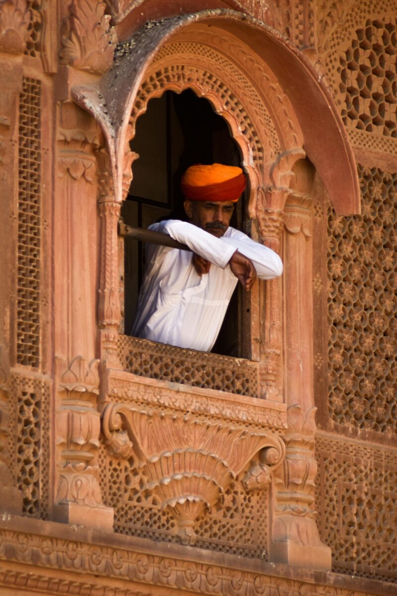 A Rajasthani man in a bright turban gazes from a historic Jodhpur window.